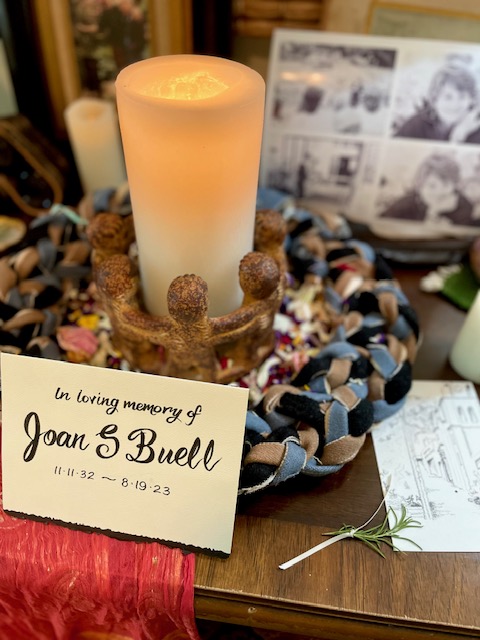 Candles, photos, and a hand-lettered sign reading: in loving memory of Joan S. Buell, 11-11-32 to 8-19-23